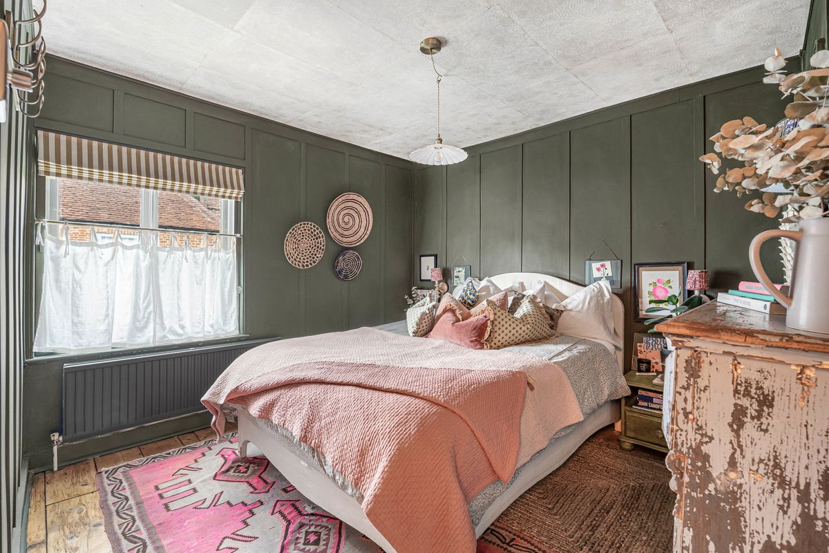 A guest room with panelled walls painted deep green and a window with a striped blind
