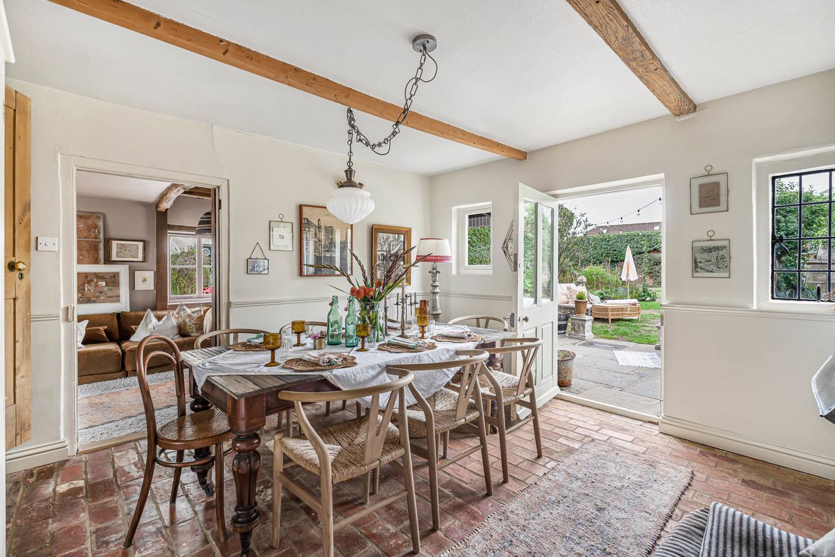 The dining room, a long table beneath beams and a door standing open to the garden