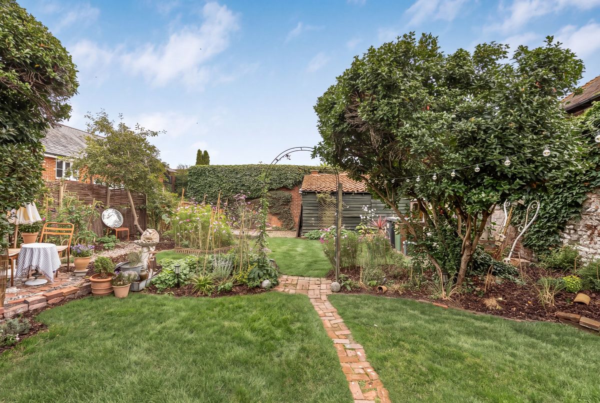 Lawns, borders and a mature tree in the walled garden, with the carport at the back